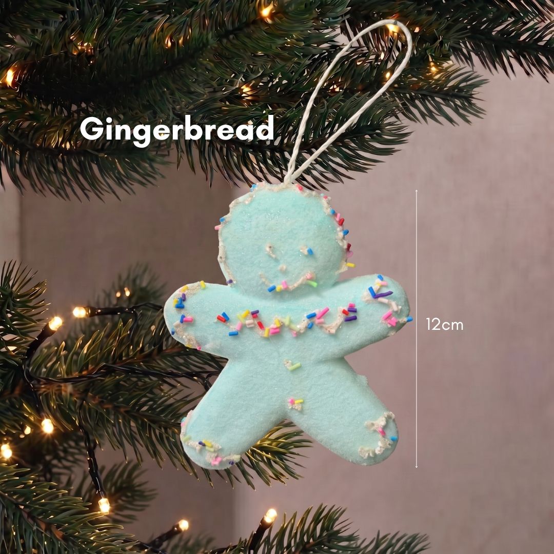 Close-up of a sweet pastel gingerbread man Christmas tree ornament hanging delicately on dark green pine branches.