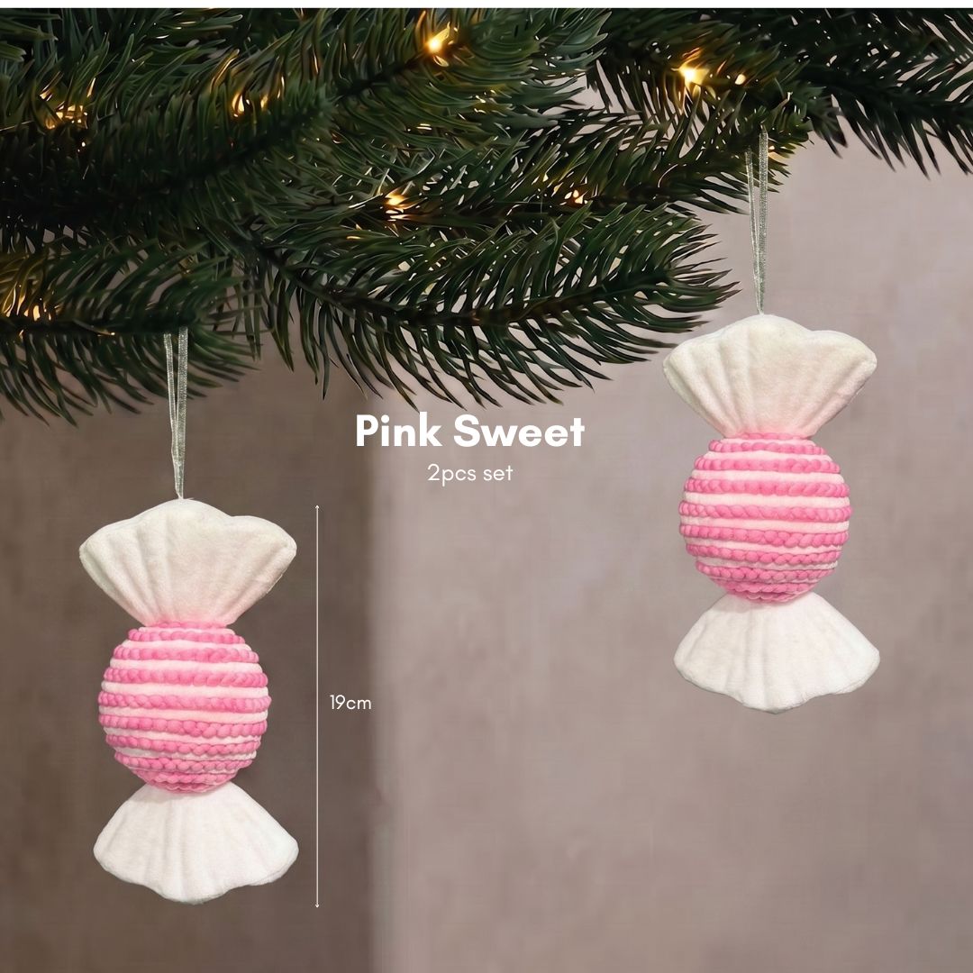 Close-up of a pastel pink sweet Christmas tree ornament hanging delicately on dark pine branches.