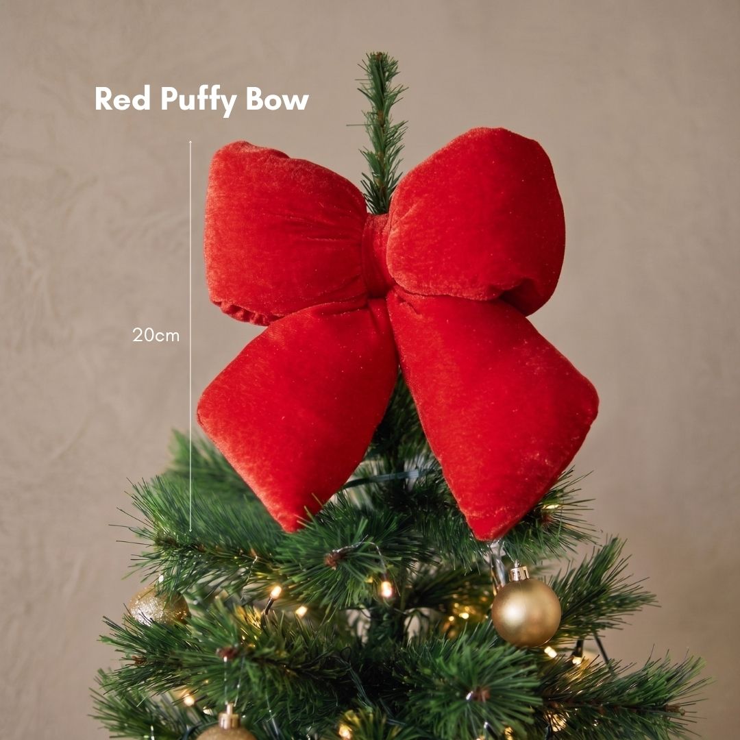 Close-up of an oversized, plush red puffy bow Christmas tree ornament nestled among dark green pine branches.