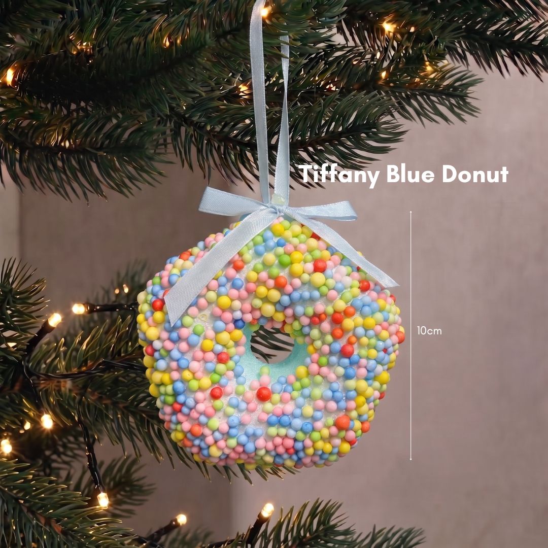 Close-up of a pastel Tiffany blue donut Christmas tree ornament with white icing swirls hanging on dark green pine branches.
