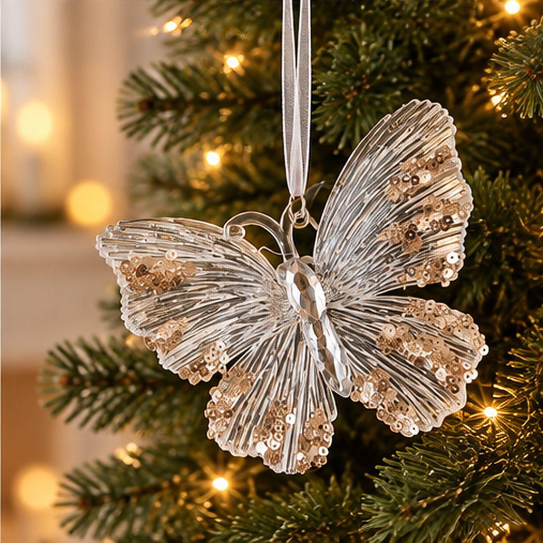 Gold and clear acrylic butterfly Christmas ornament with textured wings and sparkling gold details hanging on an artificial Christmas tree with warm lights.