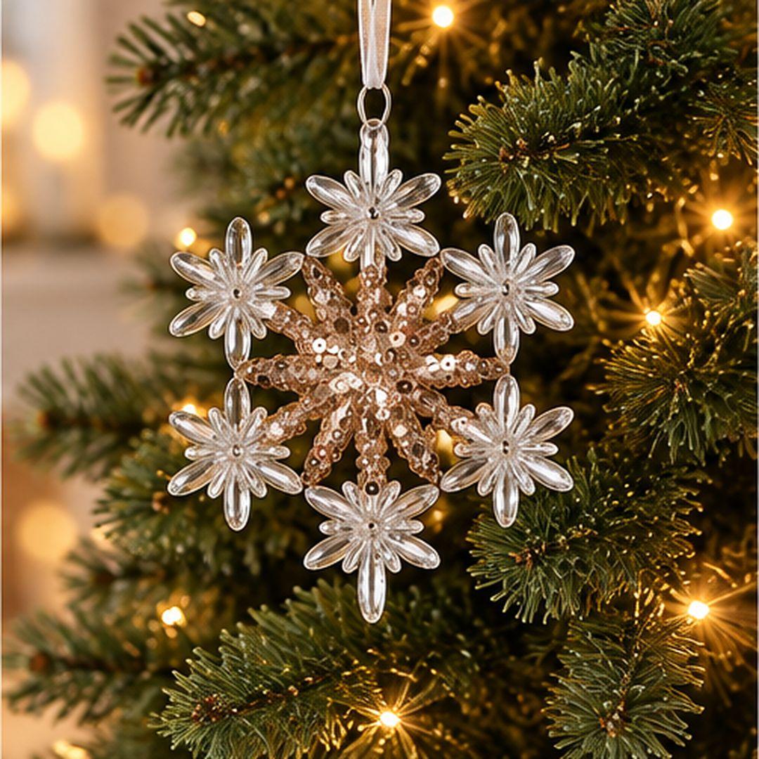 Gold and clear acrylic floral snowflake Christmas ornament with six decorative points and sparkling gold details hanging on an artificial Christmas tree.