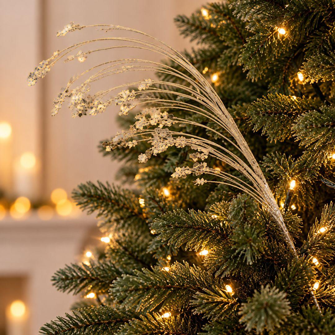 Gold glitter and sequin Christmas tree pick featuring delicate cascading branches displayed on a warm-lit artificial Christmas tree.