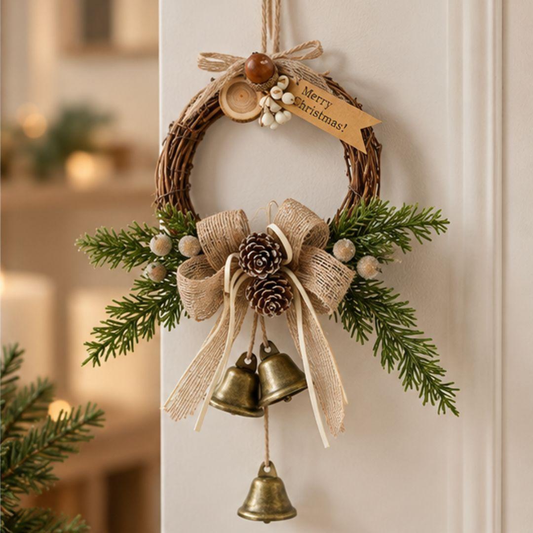 Rustic mini Christmas wreath with evergreen branches, burlap bow, pinecones and three hanging gold-tone bells displayed in a minimalist living room.