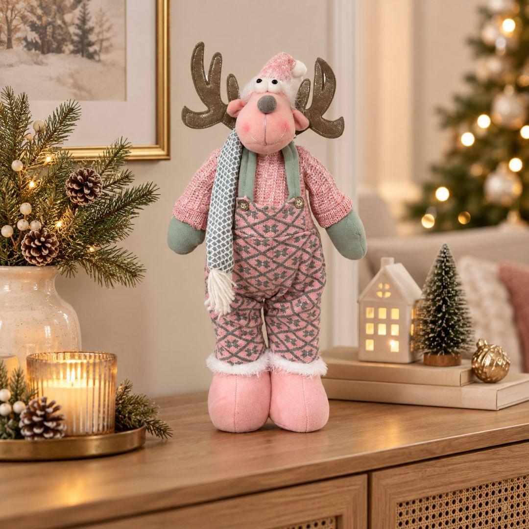 Noel Christmas Plush Design A, 43cm tall pink reindeer decoration with glittery antlers, pink patterned overalls, sage green mittens and cosy winter scarf, displayed on a wooden sideboard.