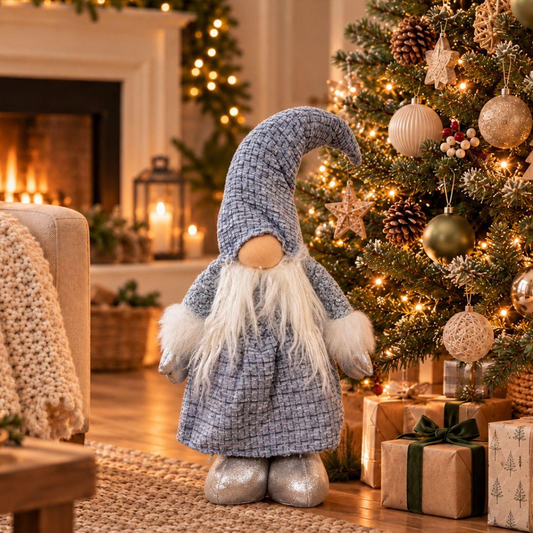 Quillby Gnome Design S featuring a textured blue outfit, curved floppy hat, fluffy white beard and silver boots, displayed beside a decorated Christmas tree.