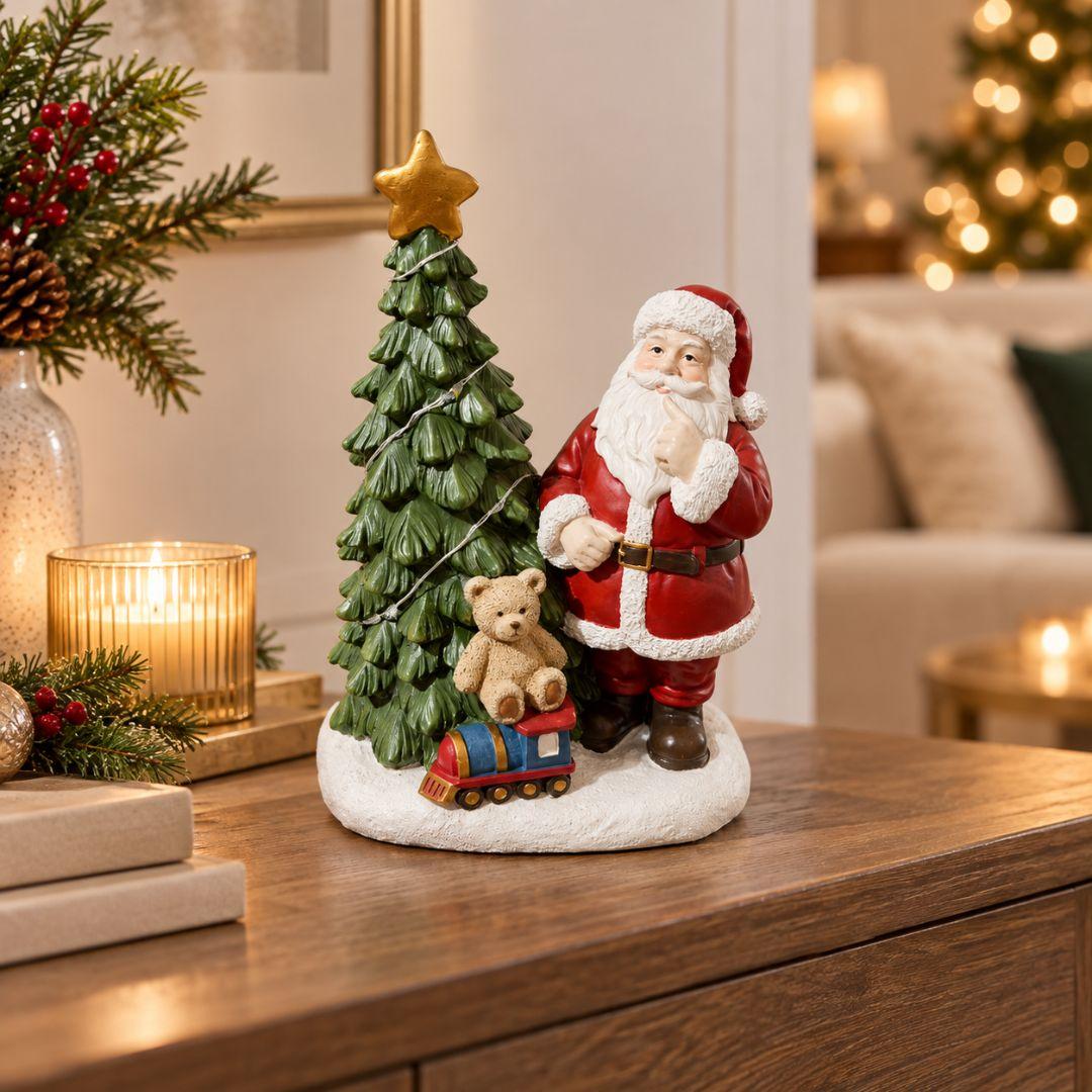 Santa's Toyland Christmas figurine with Santa Claus beside a green Christmas tree, miniature teddy bear and colourful toy train on beige background
