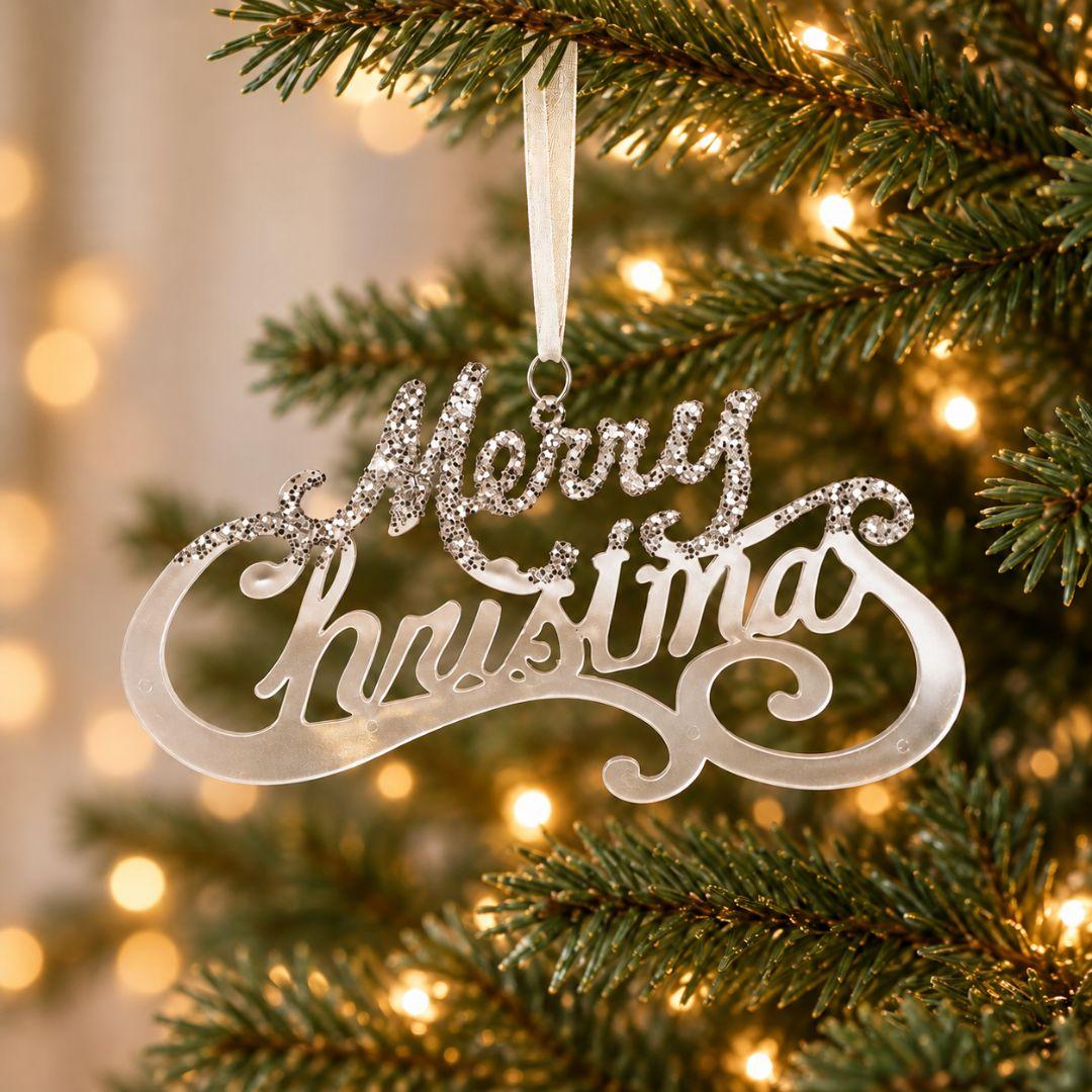 Silver acrylic Merry Christmas hanging ornament with decorative script lettering and sparkling accents displayed on an artificial Christmas tree.
