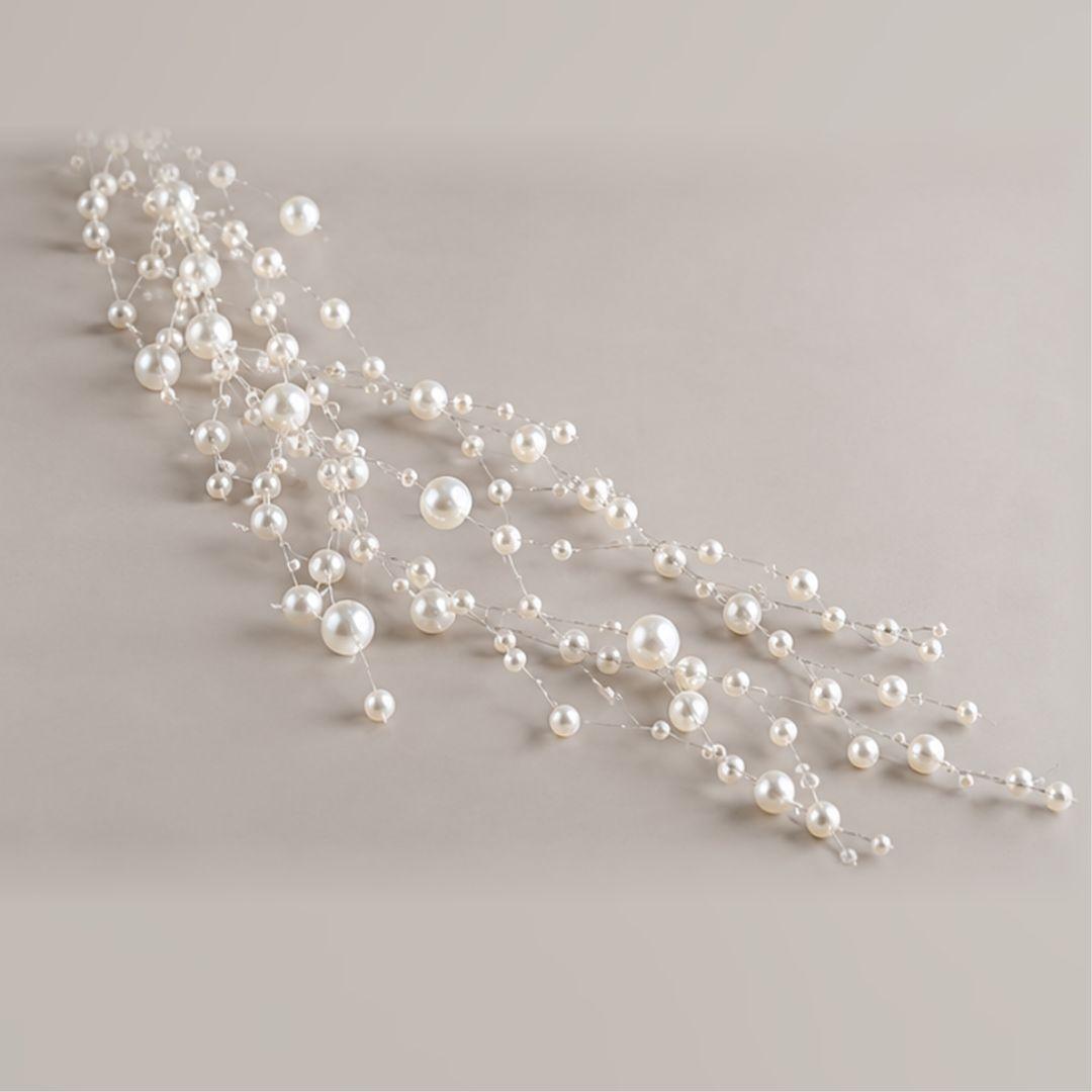 White pearl-effect beaded Christmas garland with assorted 0.3cm–0.8cm beads cascading from a warm-lit artificial Christmas tree.
