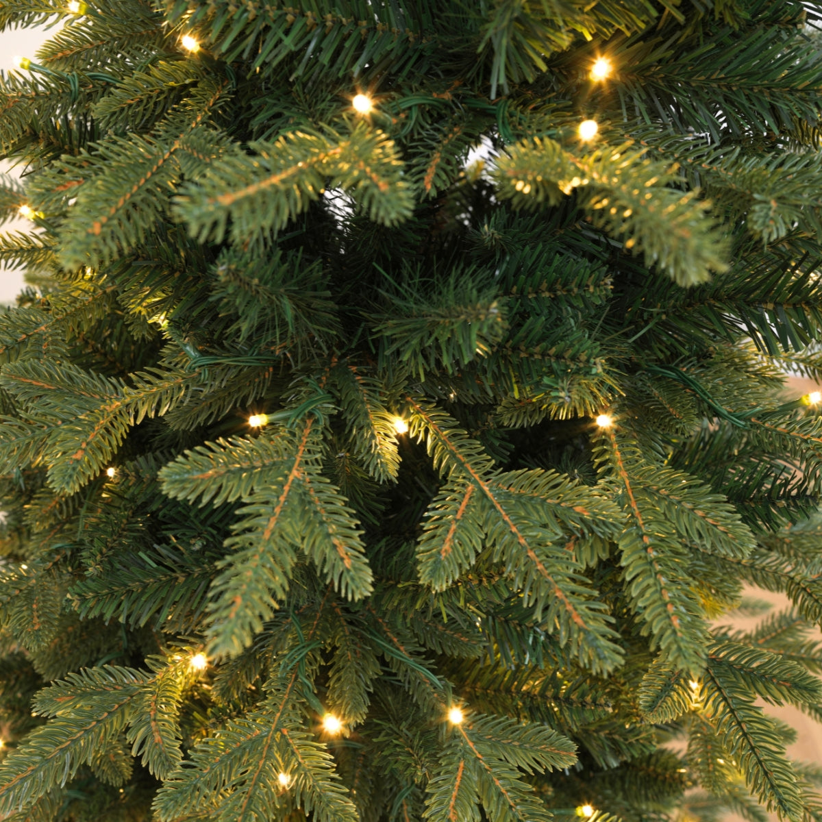Detailed close-up of dense artificial branches with integrated, glowing warm white LED lights on a space saving slim tree ideal for small homes and Christmas Tree Singapore.