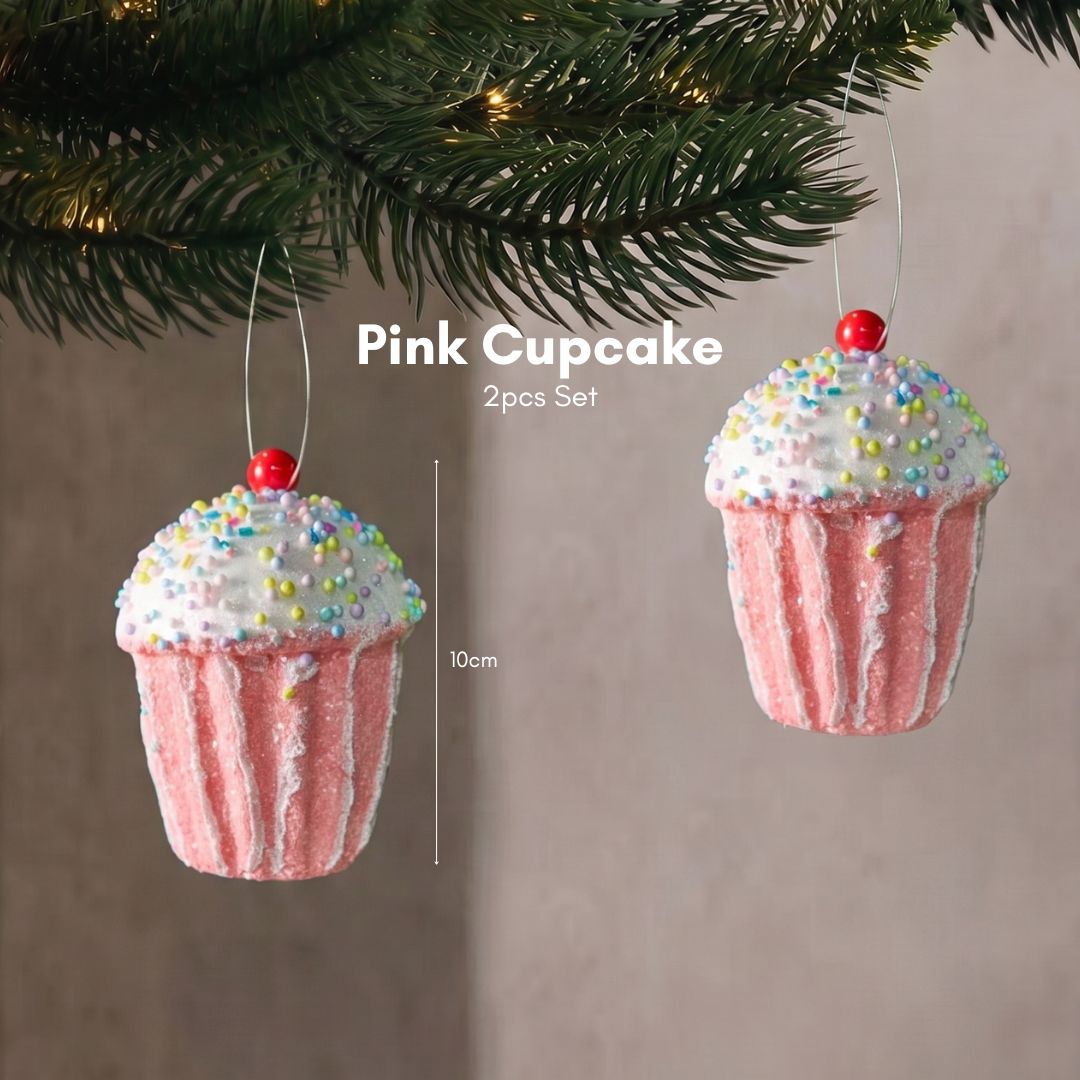 Close-up of a sweet pastel pink cupcake Christmas tree ornament with frosted details hanging delicately on dark pine branches.