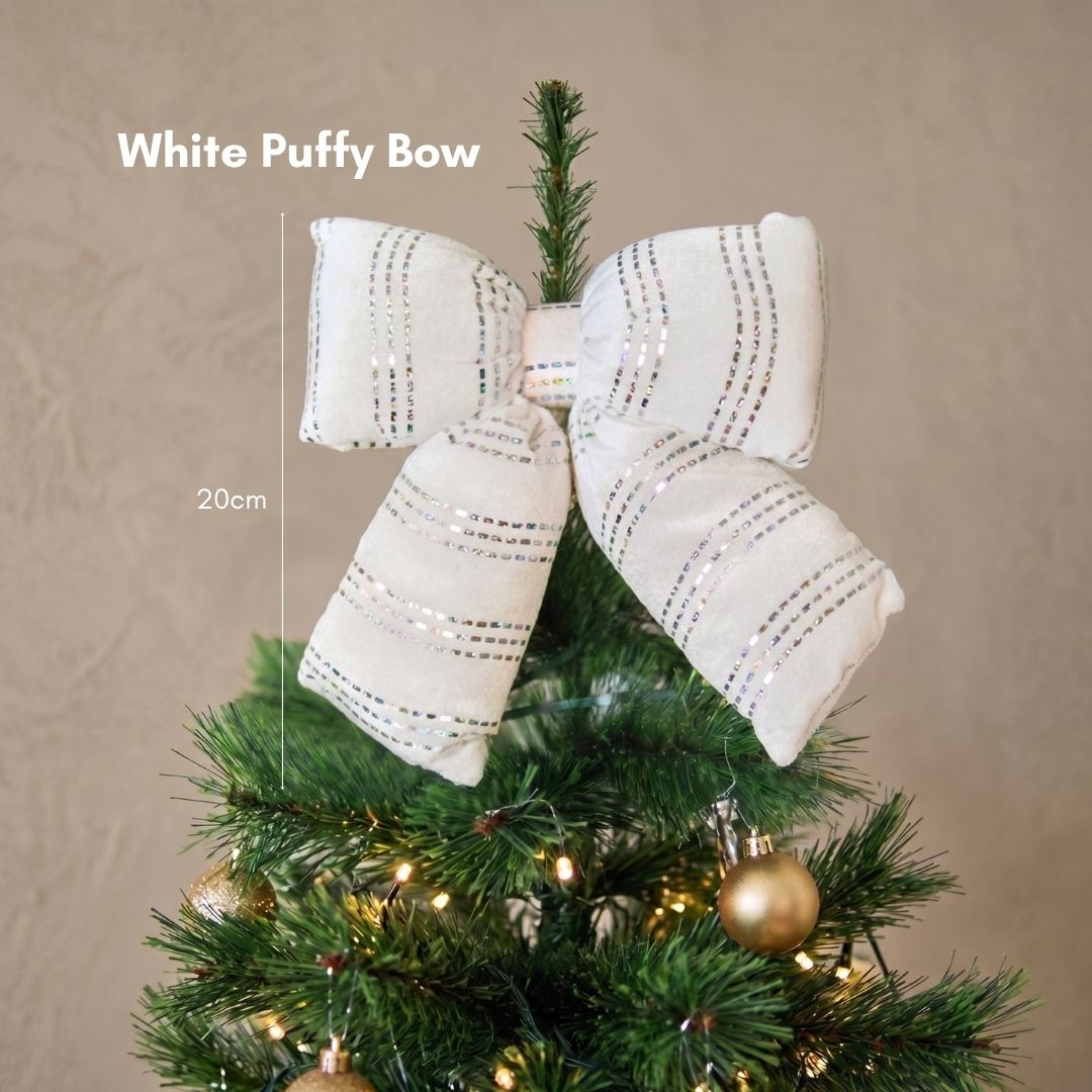 Close-up of a plush white puffy bow Christmas tree ornament catching the warm light on dark green pine branches.