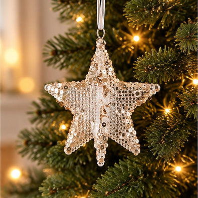 Gold acrylic five-point Christmas star ornament with delicate shimmering gold details hanging from an artificial Christmas tree with warm fairy lights.