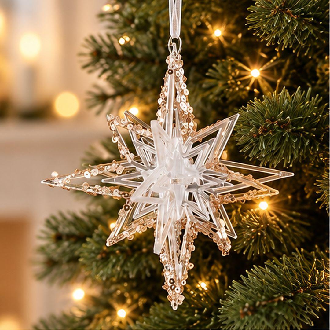 Gold and clear acrylic geometric Christmas star ornament with intricate layered points and sparkling gold details hanging on a lit Christmas tree.