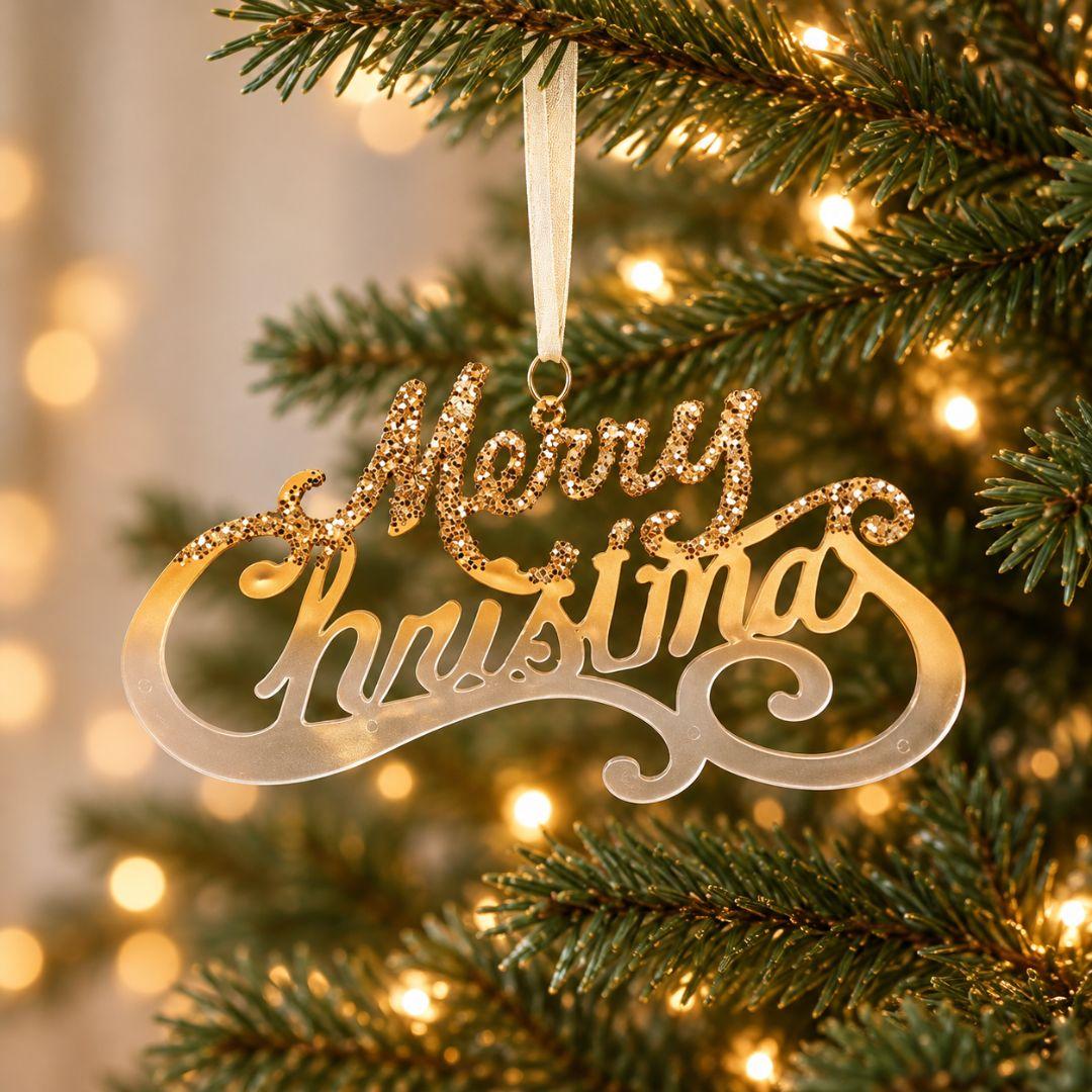 Gold acrylic Merry Christmas hanging ornament featuring elegant script lettering and sparkling gold accents displayed on an artificial Christmas tree.