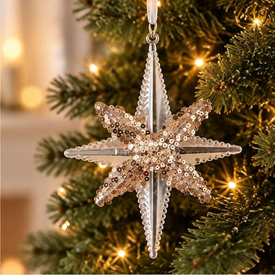 Gold and clear acrylic eight-point North Star Christmas ornament with sparkling gold embellishments hanging on an artificial Christmas tree with warm lights.