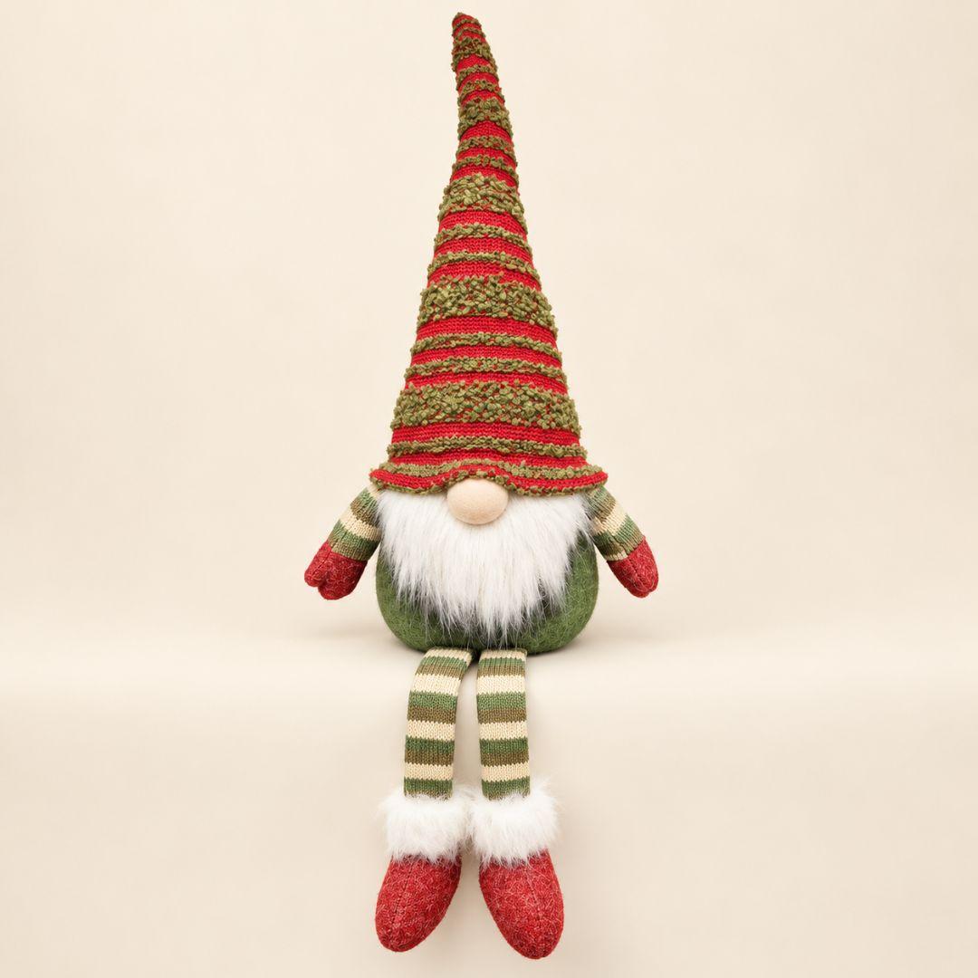 Noel sitting Christmas gnome with tall red and green knitted hat and dangling striped legs displayed on a wooden console in a cosy living room