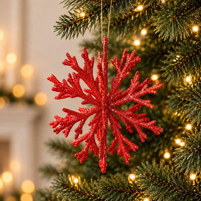 Red glitter snowflake Christmas ornament hanging on a decorated Christmas tree with warm fairy lights.