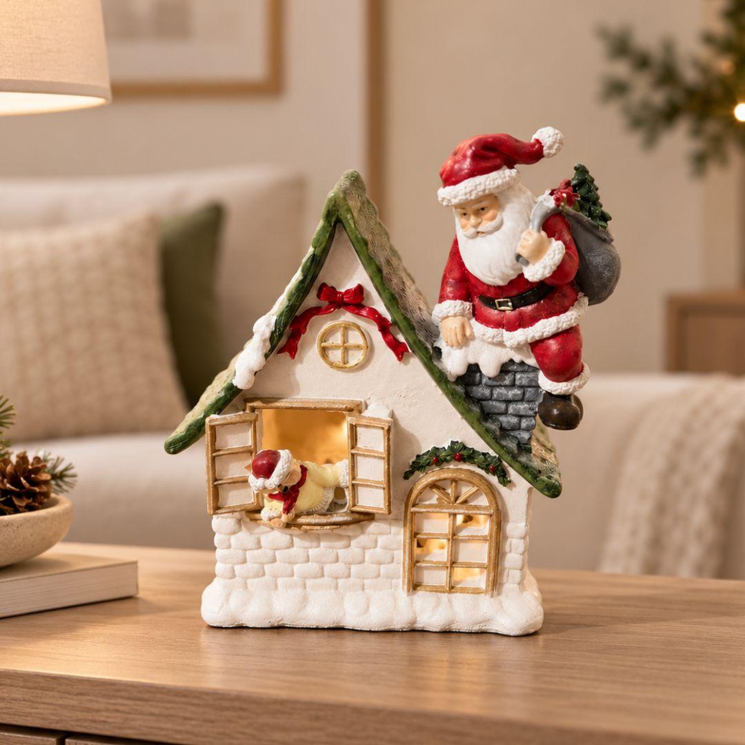 Santa's Snowy Cottage Christmas tabletop figurine with Santa on chimney, green roof and red festive ribbons on beige background