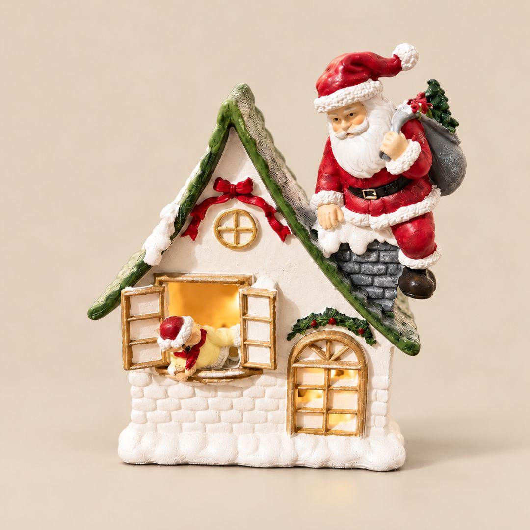Santa's Snowy Cottage Christmas tabletop figurine with Santa on chimney, green roof and red festive ribbons on beige background