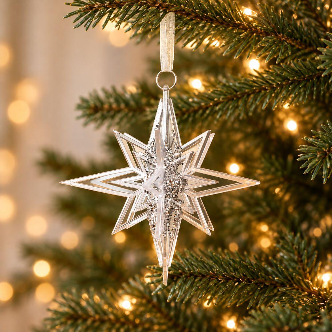 Silver and clear acrylic 3D star Christmas hanging ornament with sparkling details displayed on an artificial Christmas tree with warm fairy lights