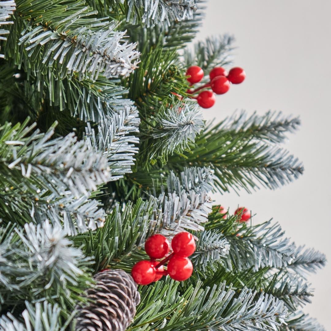 Close-up of vibrant red winter berries and natural pinecones nestled in the low-shed snowy flocking of the Speckled Space Tinker Christmas tree.